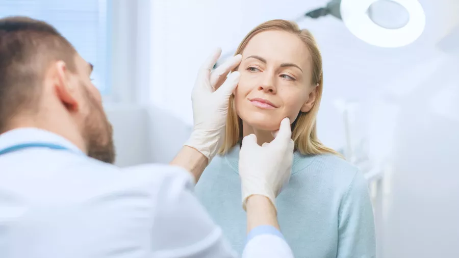 Doctor examines a patient's eye and face during a plastic surgery consultation appointment.