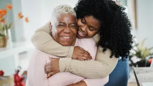 Smiling daughter hugging senior mother in the living room of home. 