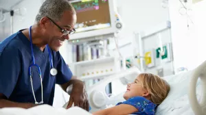 Nurse talking and laughing with pediatric inpatient lying in hospital bed.