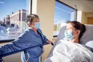 Beth Phelan, RN comforting a pre surgery patient in stretcher in hallway in Lowell General Hospital's Heart and Vascular department.