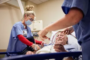 Cynthia McAndrew, RN is prepping cardiac cath lab patient before surgery with assistance from another nurse.