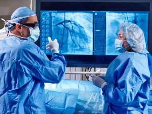 Cardiologist Omar Ali, MD, FACC in a heart and vascular surgery in Lowell General Hospital's Cath Lab talking to nurse while pointing to a large screen showing a heart scan.