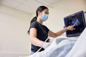 Kim-Yen Vo, Ultrasound Technologist, pointing at computer screen and talking to patient while performing ultrasound at MelroseWakefield Hospital.