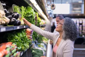 Grocery store consumer shopping for vegetables and selecting a fennel bulb to cook at home.