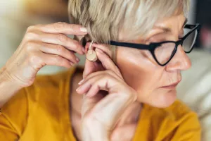 Closeup of a woman putting in a hearing aid in the comfort of her home.