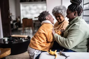 Child, with an implantable hearing device, playing with his mother and grandmother in the living room at home.