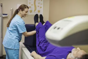 Technologist prepping patient for bone density scan in examination room.