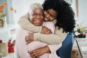 Smiling daughter hugging senior mother in the living room of home. 