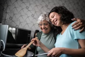 Granddaughter and grandmother happily cooking together in a home kitchen.