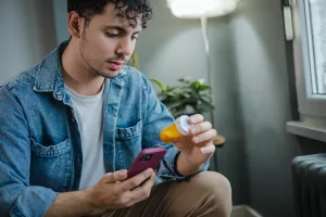 Patient reading prescription bottle at home and using phone to refill.