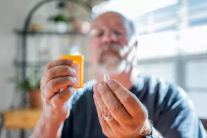 Patient reading prescription bottle and looking at pill medication in the kitchen of their home.