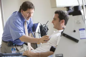 Ray Comenzo, MD (Director of Blood Bank, Transfusion and Stem Cell Services at Tufts Medical Center) examining patient during an appointment with aphoresis equipment.