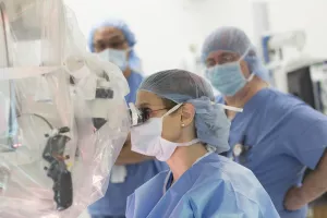 Otolaryngologist Miriam, O'Leary, MD, FACS in an ENT surgery at Tufts Medical Center looking through machine.