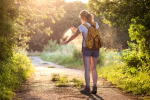 Hiking along a road in the country side during summer and spray bug repellant on.