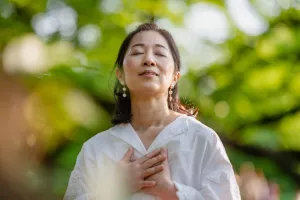 Meditating with eyes closed, hands on heart and breathing in the spring air while outside.