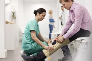 Nurse assistant helping patient put on a knee and leg brace during a clinic appointment.