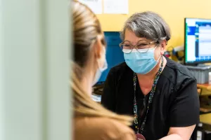 Smiling Luz Adames-Pringle, ‪phlebotomist at Tufts Medical Center, prepares a patient for a blood draw by tying band around arm.