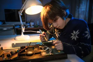 Child is playing and fixing an electronic device at their desk and using a desk light.