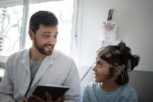 Neurologist talks to pediatric patient (prepped with wires on head) before conducting a sleep test (polysomnography). 