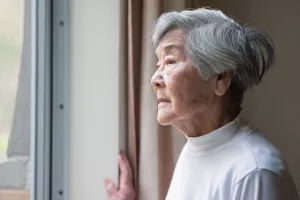 Senior looking out the window with a pensive look on face.