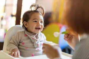 Baby smiling while eating with their caregiver.