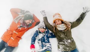 Two adults and child laying in the snow in winter clothes