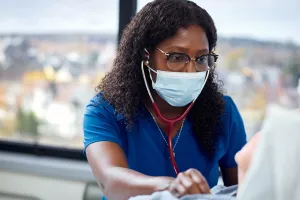 Berthine Paul, RN using a stethoscope to listen to heart of sleep apnea patient in Med 5 room at Melrose Wakefield Hospital. 