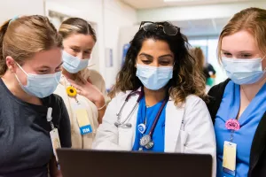 Physician Assistant, Rakhi Patel reviewing clinical information on a computer with nurses (Elizabeth Levesque, Delaney McCarthy and Fionna Donovan) in the neurology trauma unit at Tufts Medical Center. 