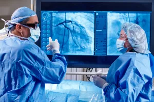 Cardiologist Omar Ali, MD, FACC in a heart and vascular surgery in Lowell General Hospital's Cath Lab talking to nurse while pointing to a large screen showing a heart scan.