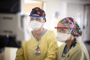 Two nurses at MelroseWakefield Hospital wearing PPE (masks, safety shields and glasses) are reviewing information on a computer.