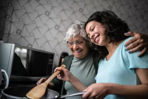 Granddaughter and grandmother happily cooking together in a home kitchen.