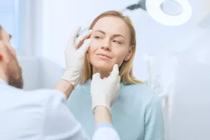 Doctor examines a patient's eye and face during a plastic surgery consultation appointment.