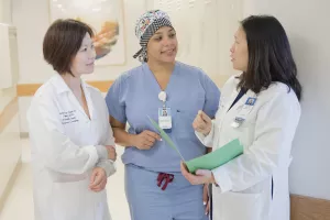 Bichchau Michelle Nguyen, MD (Director of MOHS) with Leslie Cruz, Practice Manager and Clarissa Yang, MD (Chief of Dermatology) talking in the hallway in the Dermatology clinic at Tufts Medical Center.