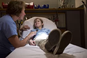 Barbara English, RN, examines pediatric patient with a stethoscope in a bay bed in the pediatric emergency room at Tufts Medical Center.