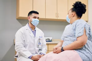 Gynecologic Oncologist Rafael Gonzalez, MD talking to patient in a hospital johnny at an appointment at Tufts Medical Center.