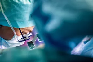 Closeup of a doctor wearing a mask and hat and looking through glasses and magnifying instruments during a surgery.