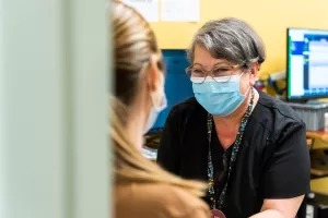 Smiling Luz Adames-Pringle, ‪phlebotomist at Tufts Medical Center, prepares a patient for a blood draw by tying band around arm.