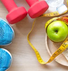 A set of hand weights, sneakers and an apple